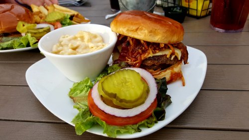 A plate featuring a burger with toppings, pickles, tomato, lettuce, and a side of macaroni and cheese.