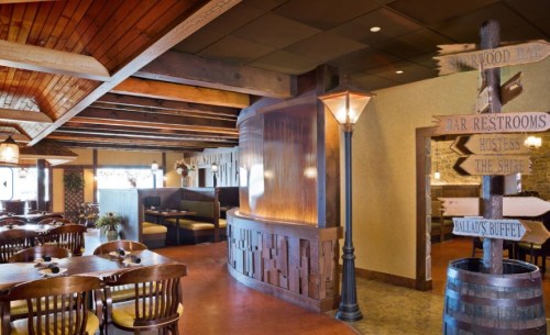 Cozy restaurant interior with wooden beams, tables, and directional signs for restrooms and dining areas.