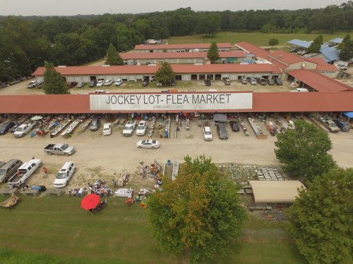 Aerial view of Jockey Lot Flea Market with vendors, parked cars, and a large sign, surrounded by greenery.
