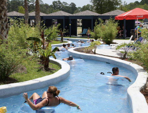 People float on inner tubes in a winding lazy river surrounded by lush greenery and shaded cabanas.