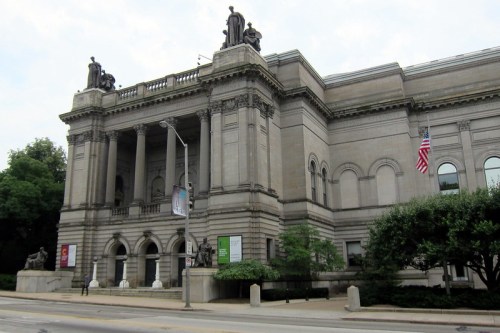 A grand museum building with classical architecture, featuring statues and banners, surrounded by greenery.