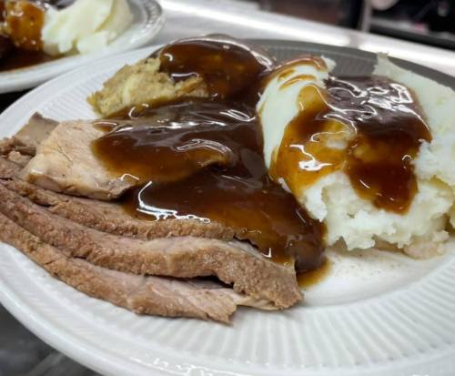 A plate of sliced roast beef with gravy, mashed potatoes, and stuffing, served on a white dish.
