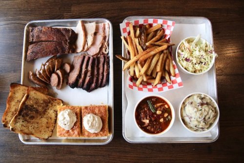 A tray with barbecue meats, sides of coleslaw, fries, baked beans, and dessert, featuring toast and pastries with cream.