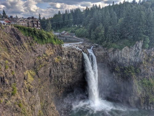 A scenic waterfall cascading down rocky cliffs, surrounded by lush greenery and a distant building.