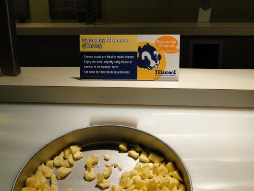 A sign about squeaky cheese curds next to a tray of freshly made cheese curds.