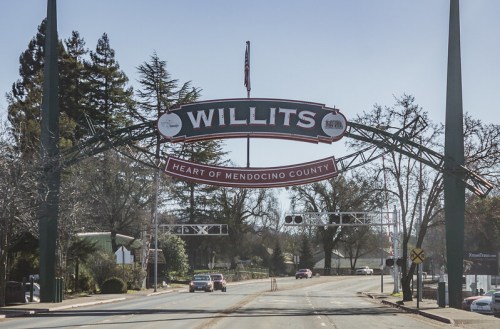 Sign archway reading "Willits" and "Heart of Mendocino County" over a street with trees and buildings in the background.