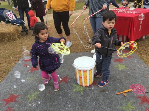 Two children play with bubble wands, creating bubbles near a bucket at an outdoor event.