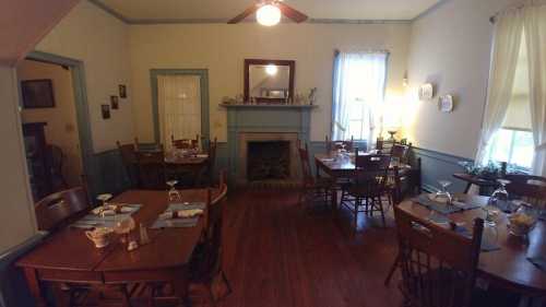 Cozy dining room with wooden tables, chairs, and a fireplace, featuring soft lighting and a welcoming atmosphere.