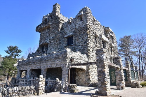 A stone castle-like structure with multiple levels, surrounded by trees and a clear blue sky.
