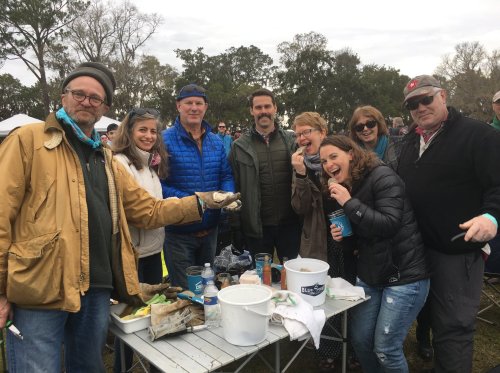 A group of eight people smiling and posing together outdoors, enjoying a gathering with food and drinks.