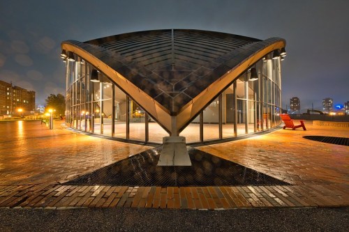 A modern building with a curved roof and large glass windows, set in an urban environment at night.