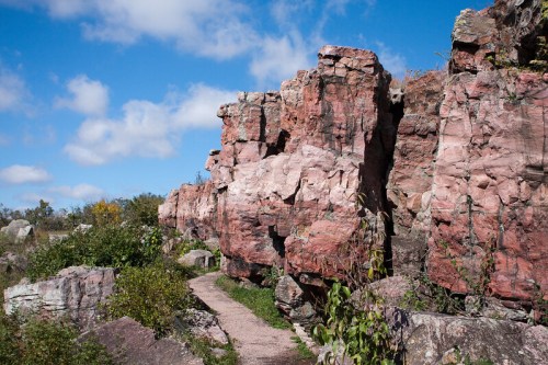 A rocky landscape with pinkish cliffs and a winding path under a blue sky with scattered clouds.