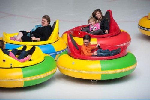 A group of people enjoying bumper cars on ice, smiling and having fun in colorful, circular vehicles.