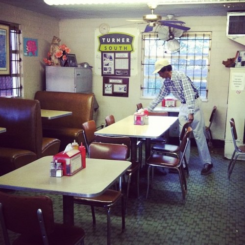 A diner interior with empty booths and tables, featuring a man setting a table in a cozy, retro atmosphere.