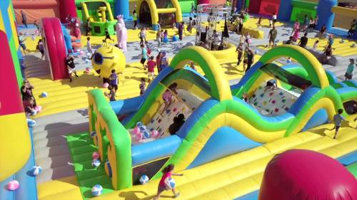 A vibrant inflatable playground filled with children playing on slides and bouncing, surrounded by colorful structures.
