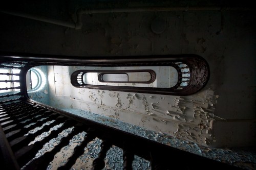 A spiral staircase with peeling paint and a circular window at the bottom, creating a sense of depth and decay.
