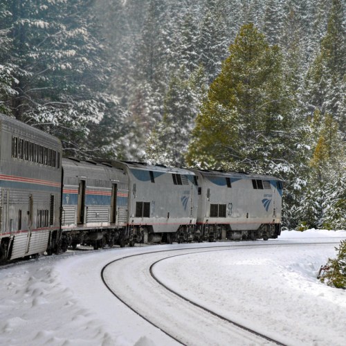 A train curves through a snowy landscape, surrounded by evergreen trees and a serene winter atmosphere.
