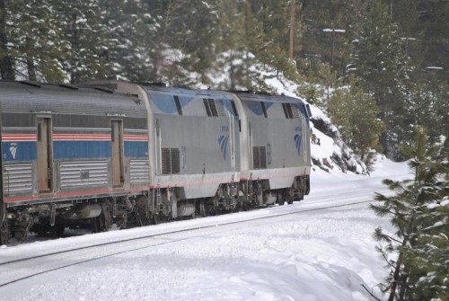 A train travels through a snowy landscape, surrounded by trees and a winter scene.