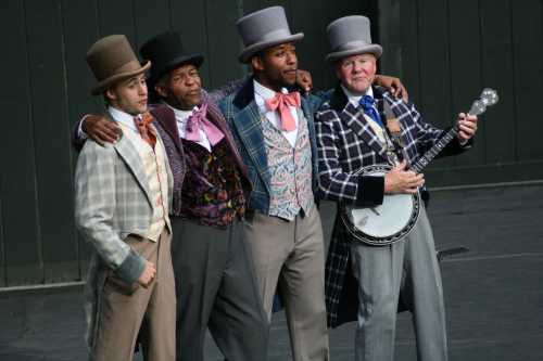 Four men in colorful, vintage attire stand together on stage, smiling and posing, with one holding a banjo.