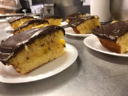 Slices of yellow cake topped with chocolate frosting, served on white paper plates.