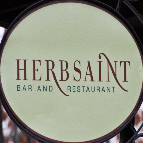 Sign for "Herbsain" Bar and Restaurant, featuring elegant lettering on a light green background.