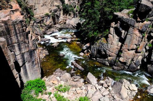 A scenic view of a river flowing through rocky cliffs, surrounded by lush greenery and clear blue water.