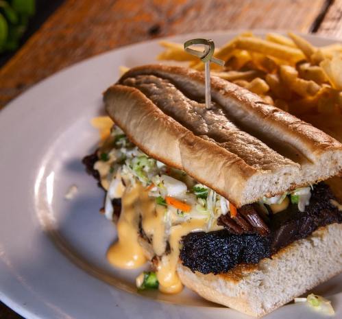 A close-up of a sandwich filled with meat and cheese, served with a side of fries on a white plate.
