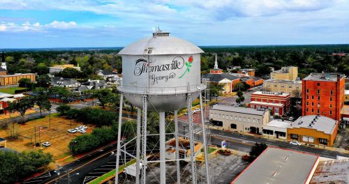 Aerial view of the Thomasville, Georgia water tower surrounded by buildings and greenery under a cloudy sky.