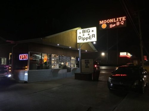 A brightly lit diner named "Big Dipper" at night, with an "Open" sign and nearby BBQ restaurant signage.