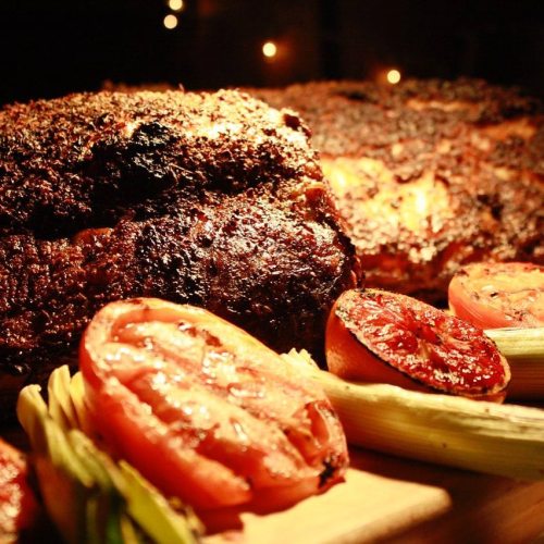 A close-up of roasted meat with charred tomatoes and green onions, illuminated by soft, warm lighting.