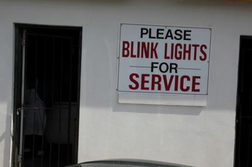 Sign on a wall reads "PLEASE BLINK LIGHTS FOR SERVICE" with a door visible in the background.