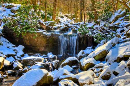 A serene winter scene featuring a small waterfall surrounded by snow-covered rocks and trees.