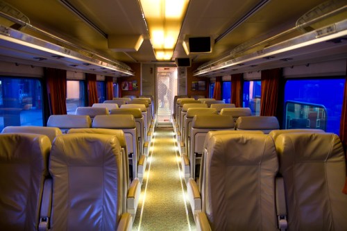 Interior of a train carriage featuring rows of leather seats and soft lighting along the aisle.