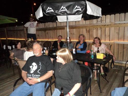 A group of people sitting under an umbrella on a patio, enjoying drinks and socializing at night.