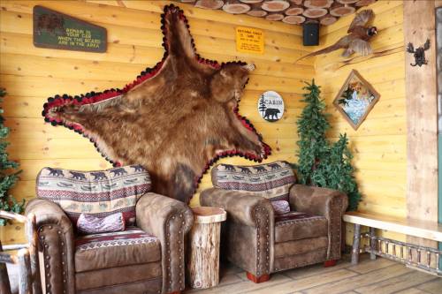 Cozy cabin interior with two leather chairs, a bear skin rug on the wall, and rustic decor including pine trees.
