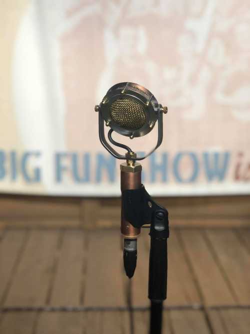 A vintage microphone on a stand, set against a blurred background with the words "BIG FUN SHOW."