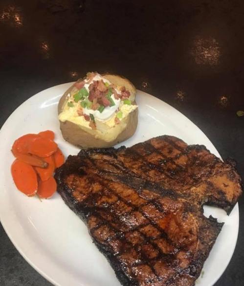 A plate featuring a grilled steak, baked potato with toppings, and sliced carrots.