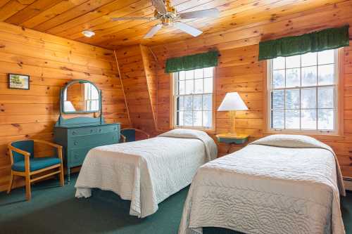 Cozy wooden bedroom with two twin beds, a dresser, and large windows letting in natural light.