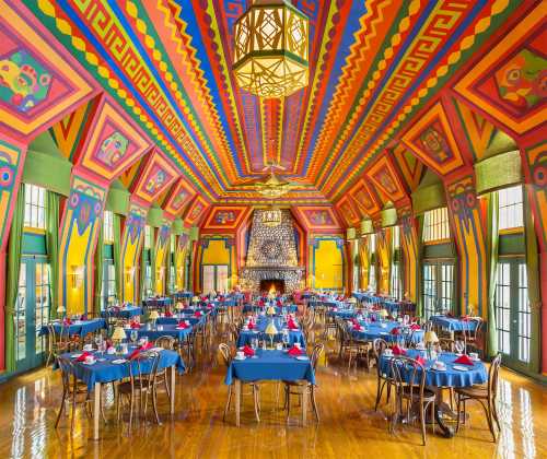 Vibrant dining room with colorful patterned walls, blue tables, and a large chandelier, creating a lively atmosphere.