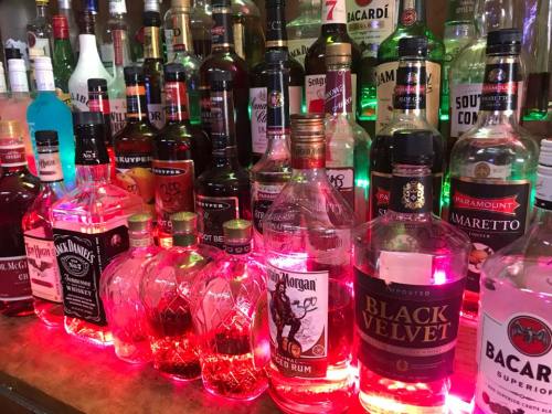 A colorful display of various liquor bottles illuminated with pink and green lights on a bar shelf.