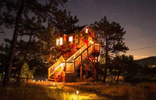 A brightly lit treehouse at night, surrounded by trees and a starry sky, with a staircase leading up to it.