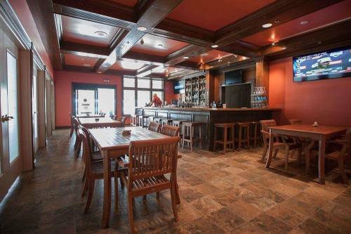 Interior of a restaurant featuring wooden tables, a bar, and red walls, with a TV and large windows for natural light.