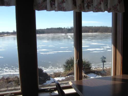 View of a frozen lake through large windows, with snow-covered ground and a clear blue sky in the background.