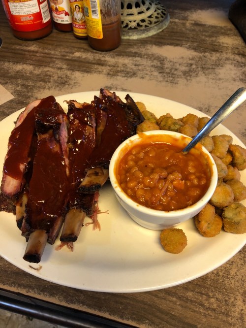 A plate featuring BBQ ribs with sauce, baked beans in a bowl, and a side of fried okra.