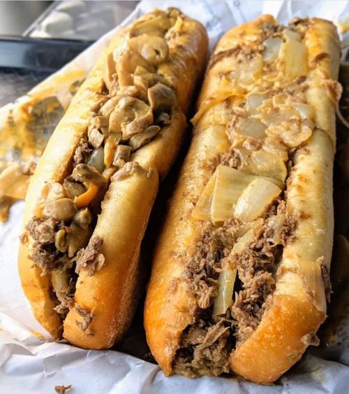 Two loaded sandwich rolls filled with shredded meat, sautéed onions, and mushrooms, served on a paper-lined tray.