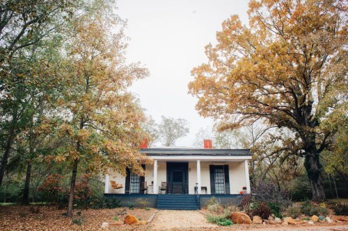 A charming white house surrounded by autumn trees with orange and yellow leaves, set in a serene landscape.