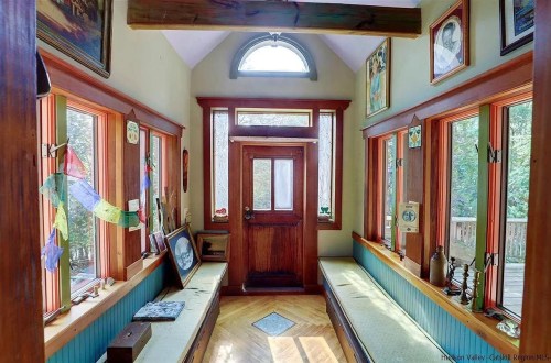 Bright entryway with large windows, wooden accents, and benches, featuring artwork and decorative items.