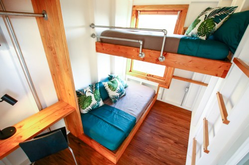 Cozy interior of a tiny home featuring a bunk bed, a sofa, and a workspace with wooden accents and tropical-themed cushions.