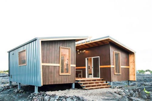 Modern two-tone house with wooden accents, set on rocky terrain, featuring a welcoming entrance and large windows.