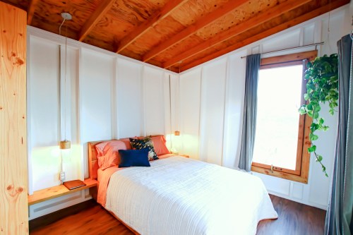 Cozy bedroom with a double bed, wooden accents, natural light, and a hanging plant by the window.